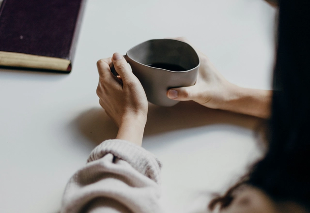 Woman sitting at a table holding grey mug